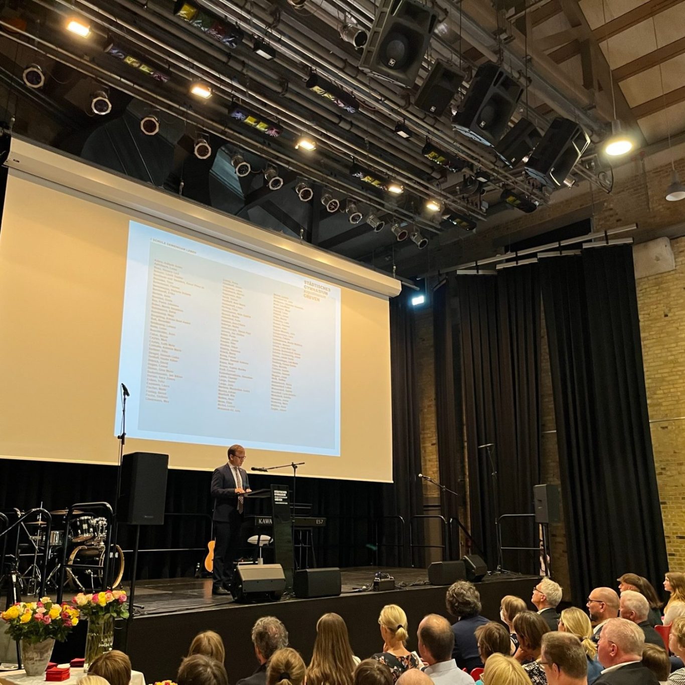 Ballenlager Greven Zeugnisvergabe Ein Redner steht auf der Bühne vor einem Publikum in einem großen Veranstaltungsraum.